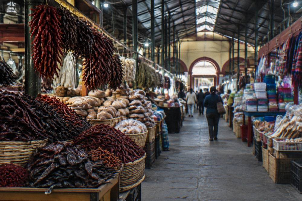 A busy covered market hall in Oaxaca with stalls of chillies, bread and household goods