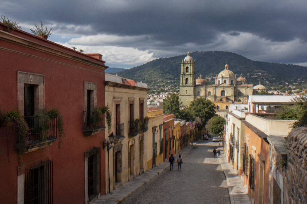 Dark storm clouds gathering over Oaxaca rooftops with sunlit church domes below