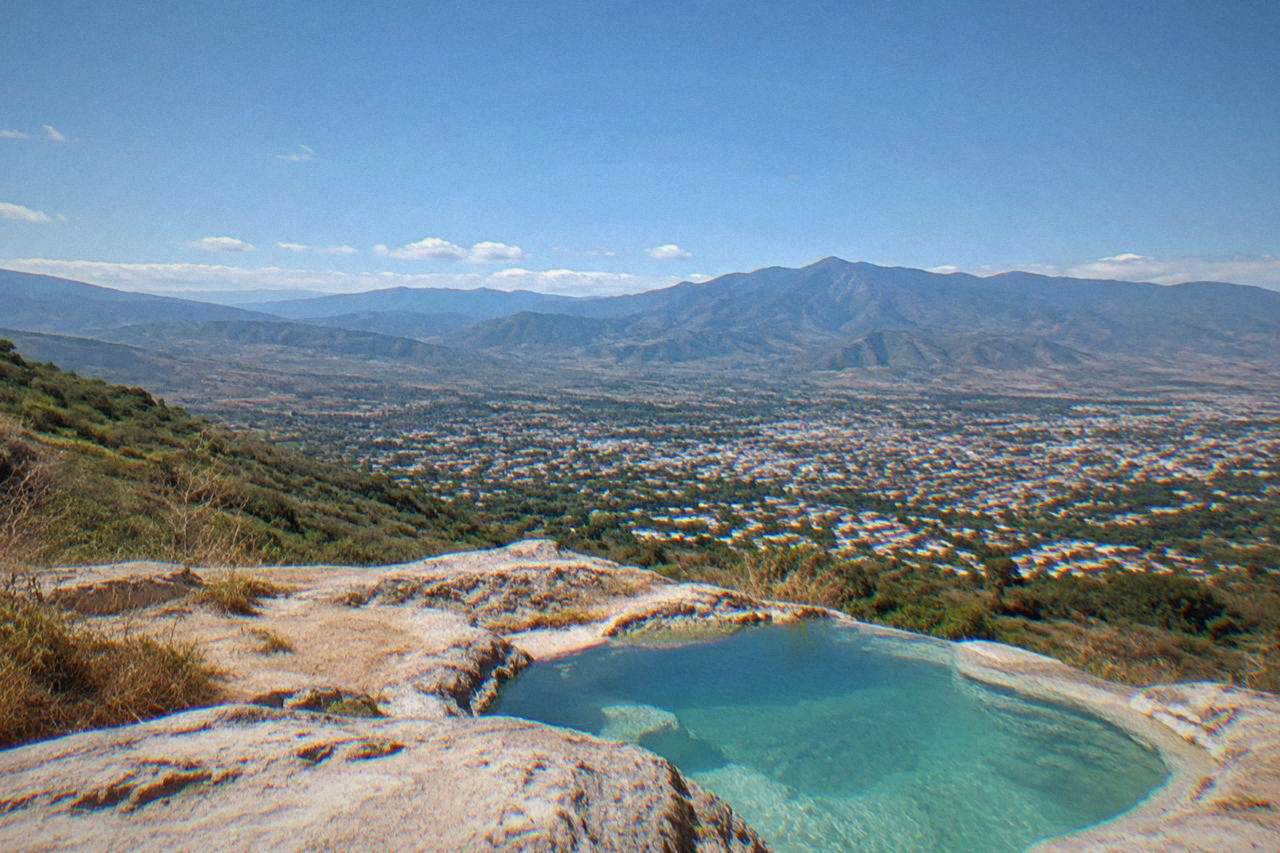 Green mountain valley under a blue sky with the city of Oaxaca spread below