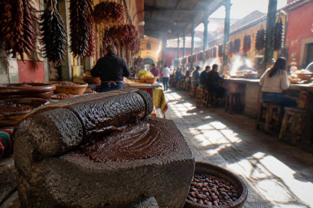 A stone mill grinding cacao beans into dark paste at a market counter