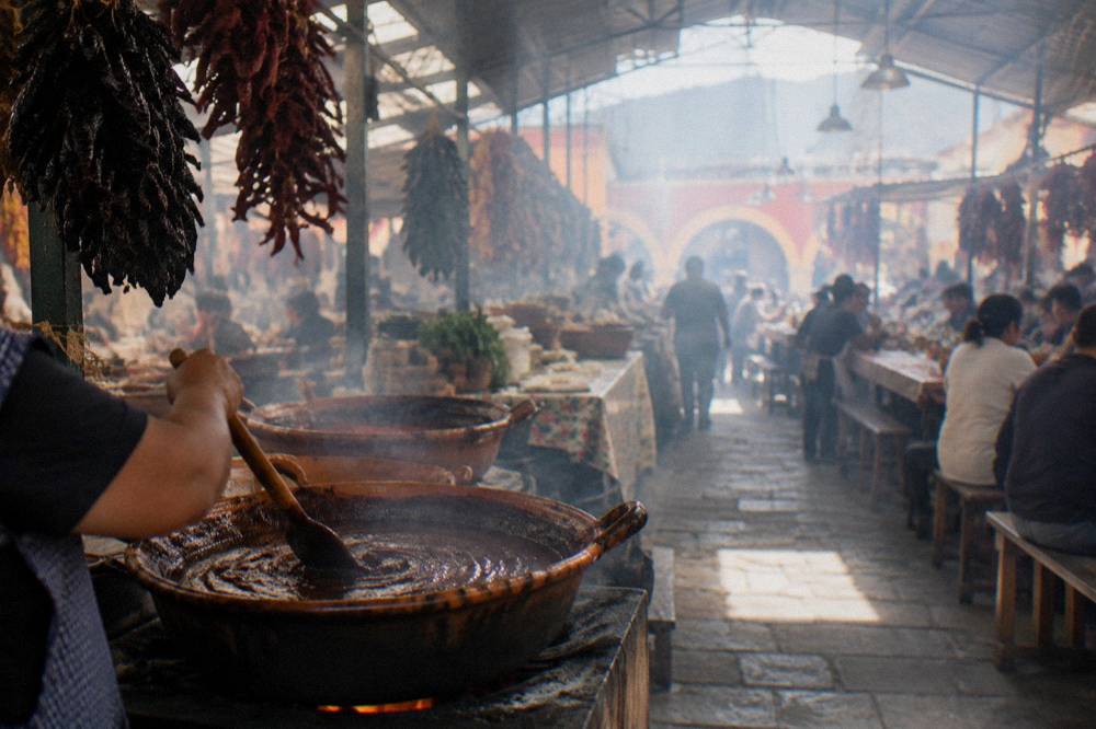 A dark mole sauce being stirred in a clay pot on a stove
