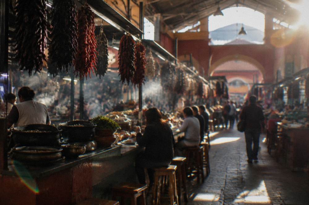 A busy food market hall with stallholders serving plates to customers