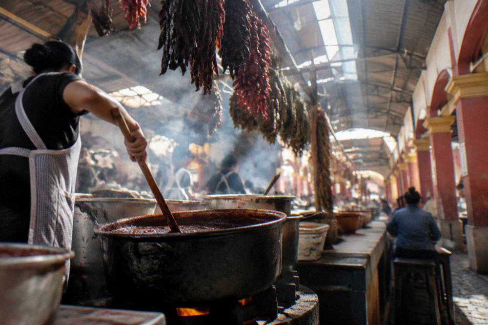 A cook stirring a large pot of dark sauce over a stove