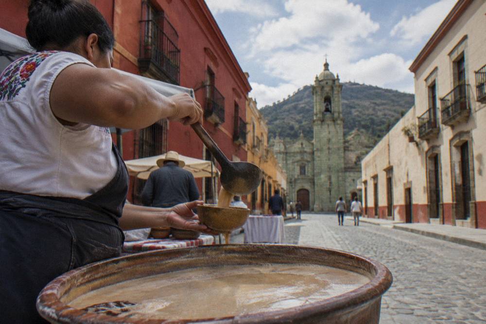 A vendor ladling tejata from a large basin in a Oaxaca market