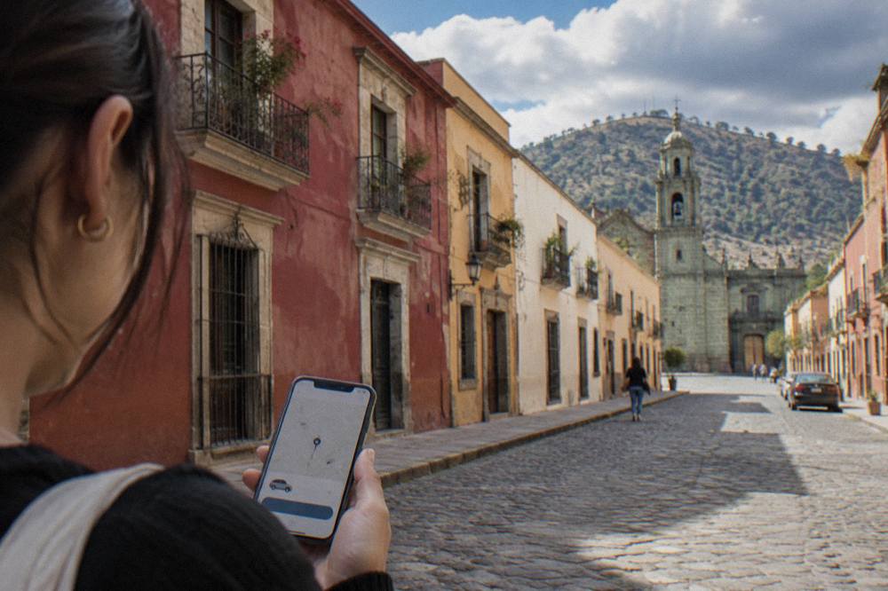 A phone showing a ride-hailing app map over a sunlit Oaxaca street corner