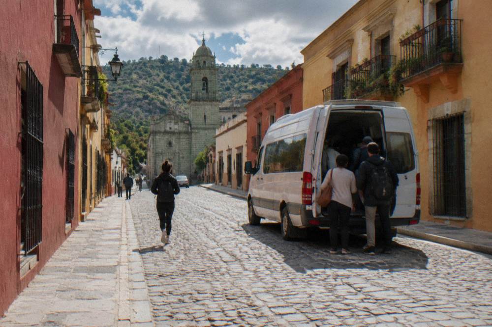 A shared van colectivo loading passengers at a street-side departure point in Oaxaca