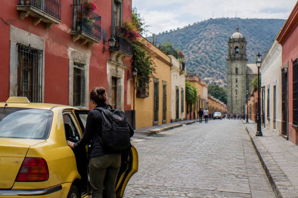 A traveller with a backpack closing a taxi door outside a colonial hotel in Oaxaca