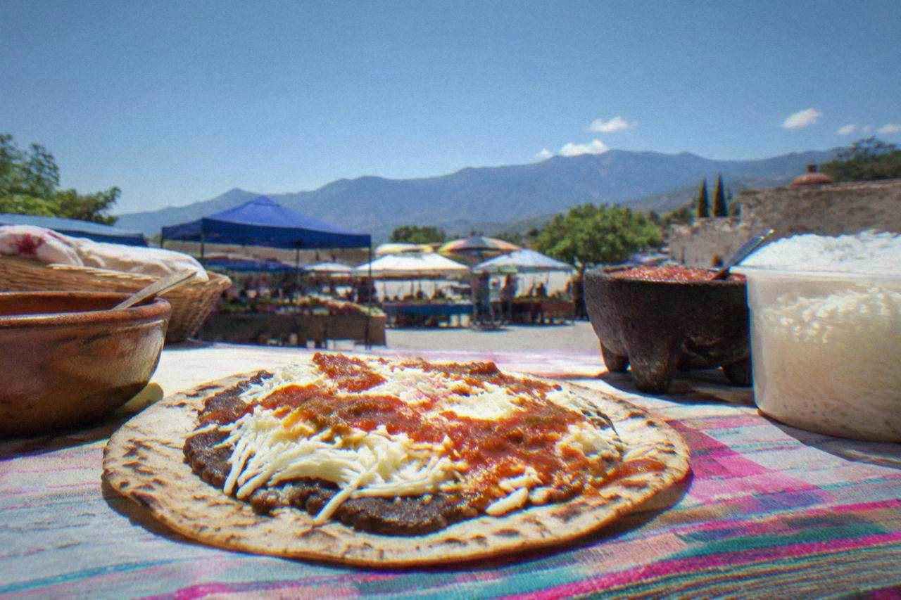 A large toasted tortilla topped with beans, quesillo and salsa on a market stall counter in Oaxaca