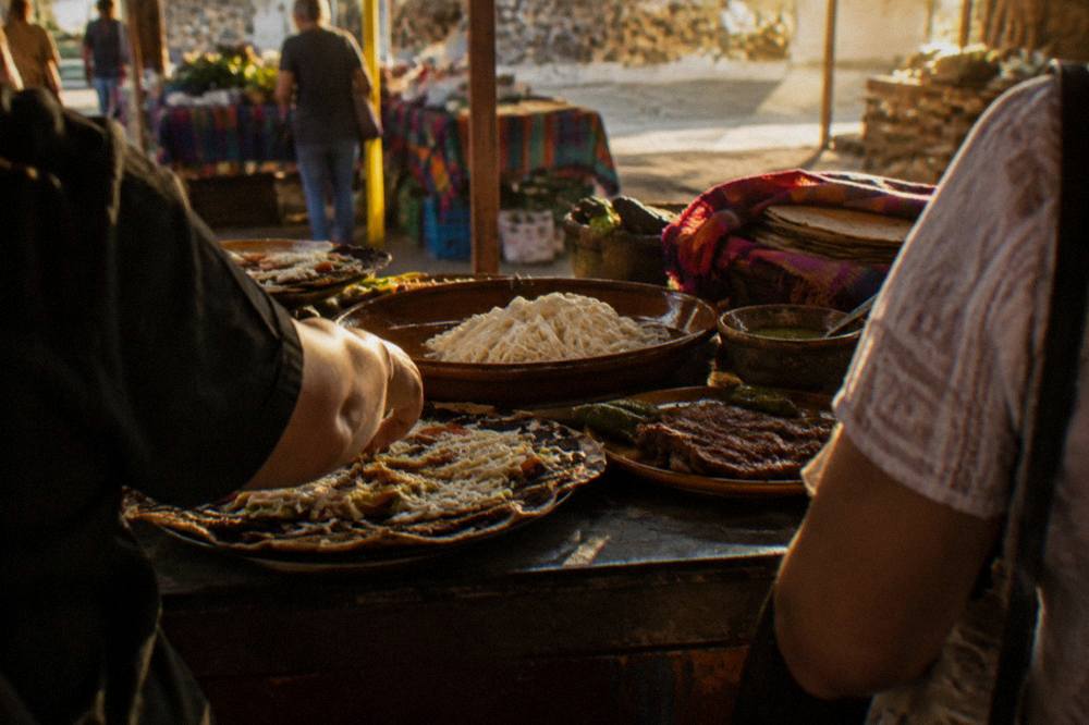 Travellers and a local guide tasting dishes at a market stall in Oaxaca City