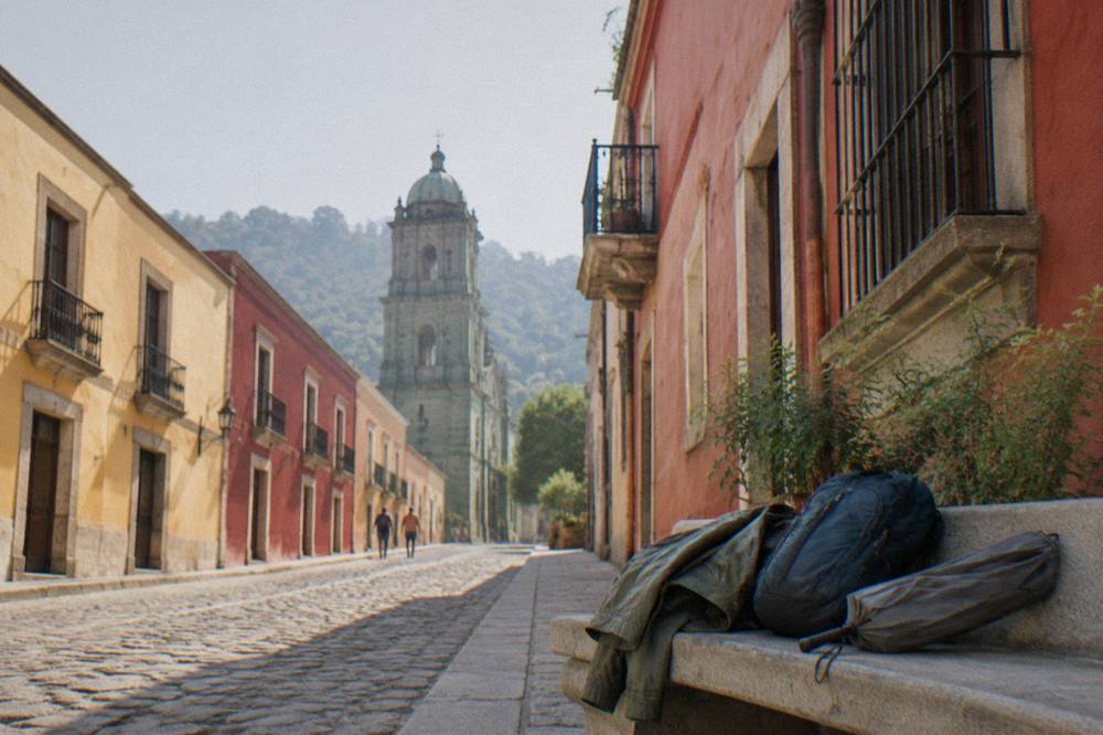 A light rain jacket and compact umbrella resting on a courtyard bench beside a daypack