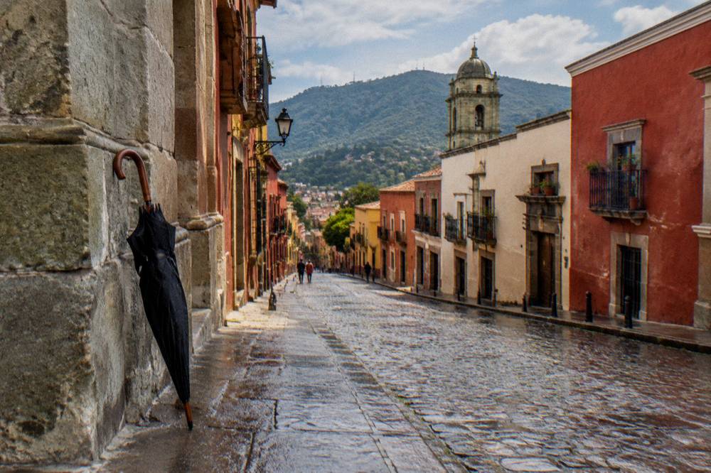 An umbrella leaning against a colonial stone wall on a wet street after rain