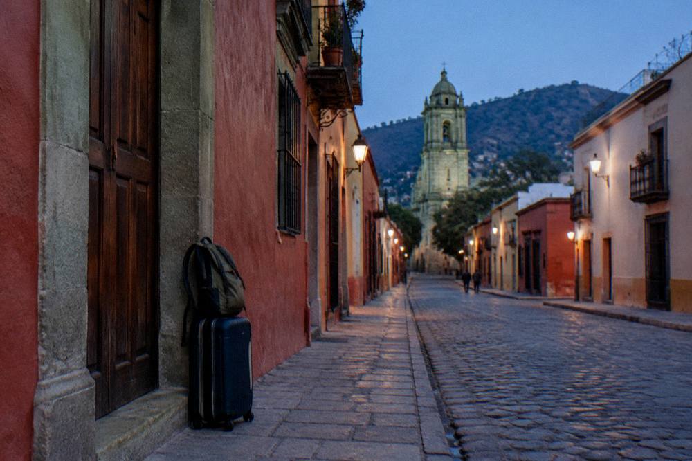 A suitcase closed and standing by a door with a daypack slung on top, ready to leave for the airport