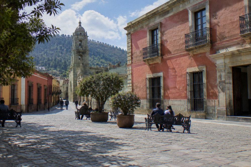A stone-paved plaza outside a museum building in central Oaxaca with people resting on benches