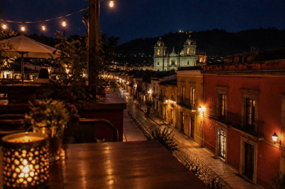 Rooftop tables and string lights overlooking the lit church towers of Oaxaca City's historic centre