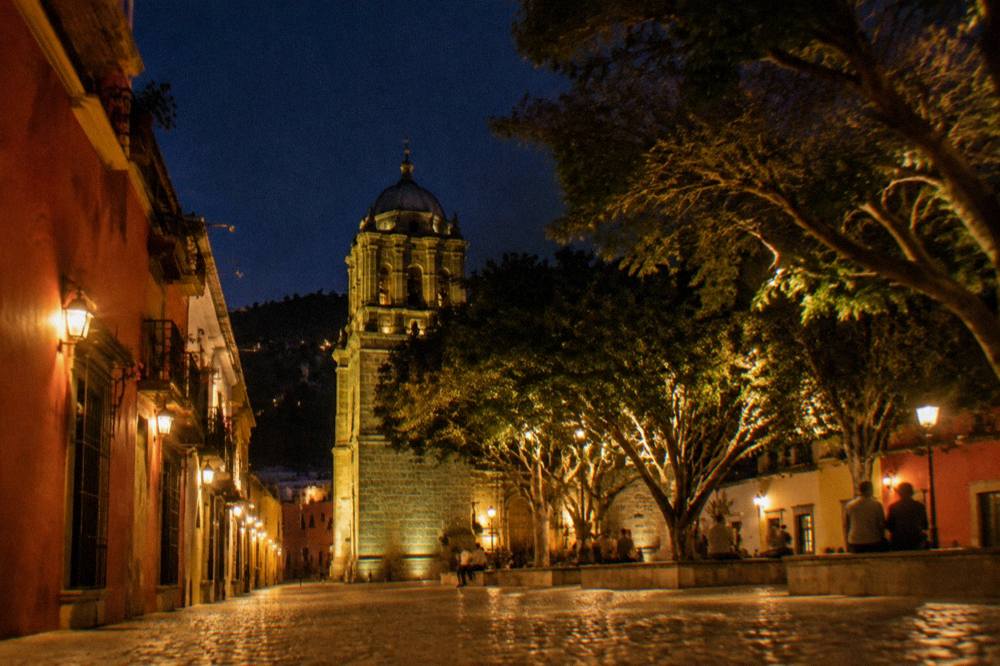 A plaza in Oaxaca City at night with lit trees and people seated around the edges