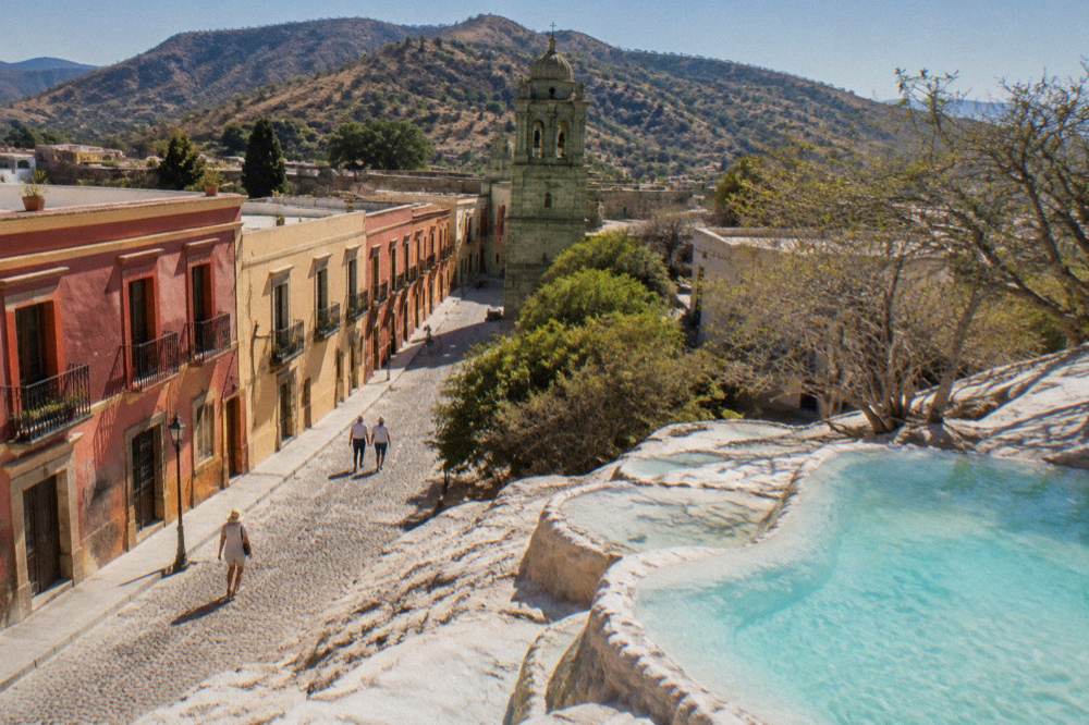 Mineral terraces and turquoise pools at a mountain spring site above a valley