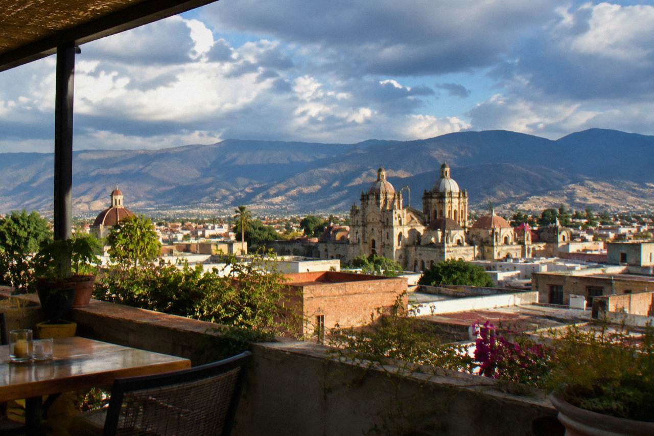 View over the rooftops and church domes of Oaxaca City toward surrounding mountains at late afternoon