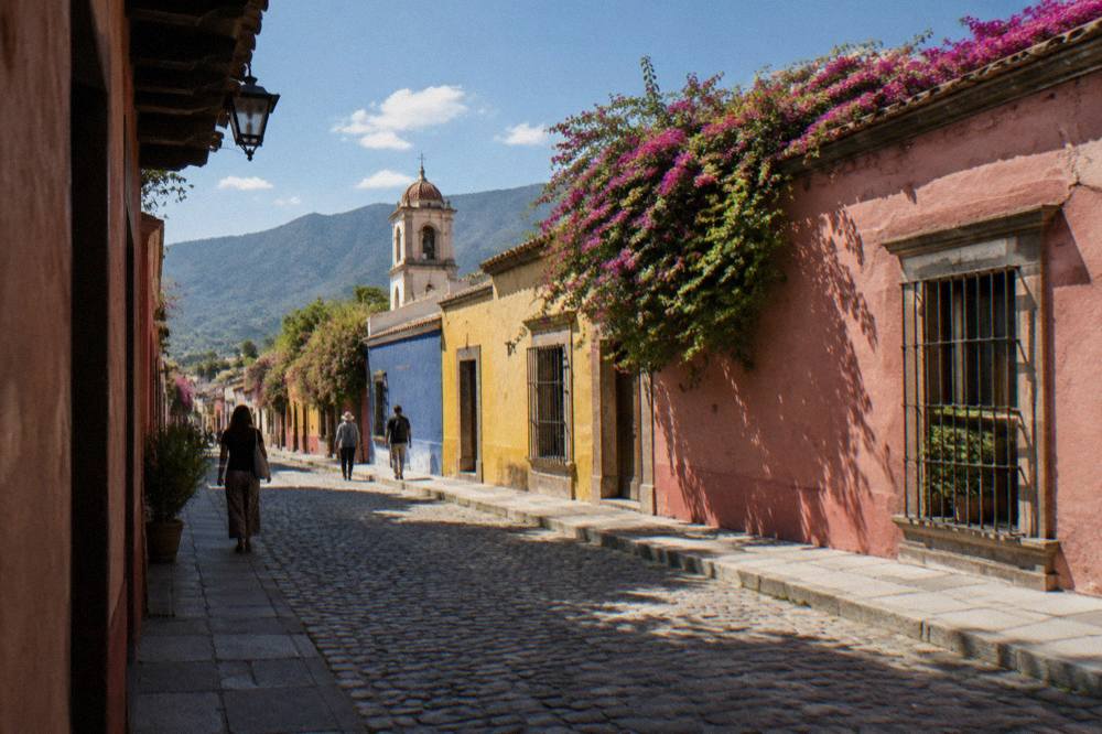 A shaded colonial street in Oaxaca City with brightly painted walls and pedestrians walking