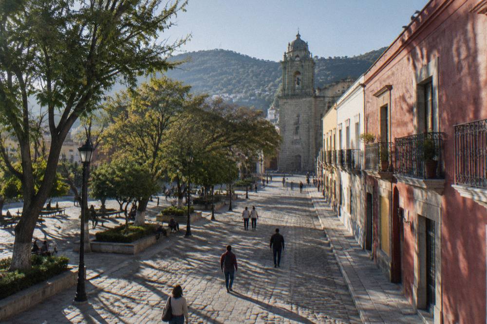 Plaza in Oaxaca City with trees, arcades and people walking