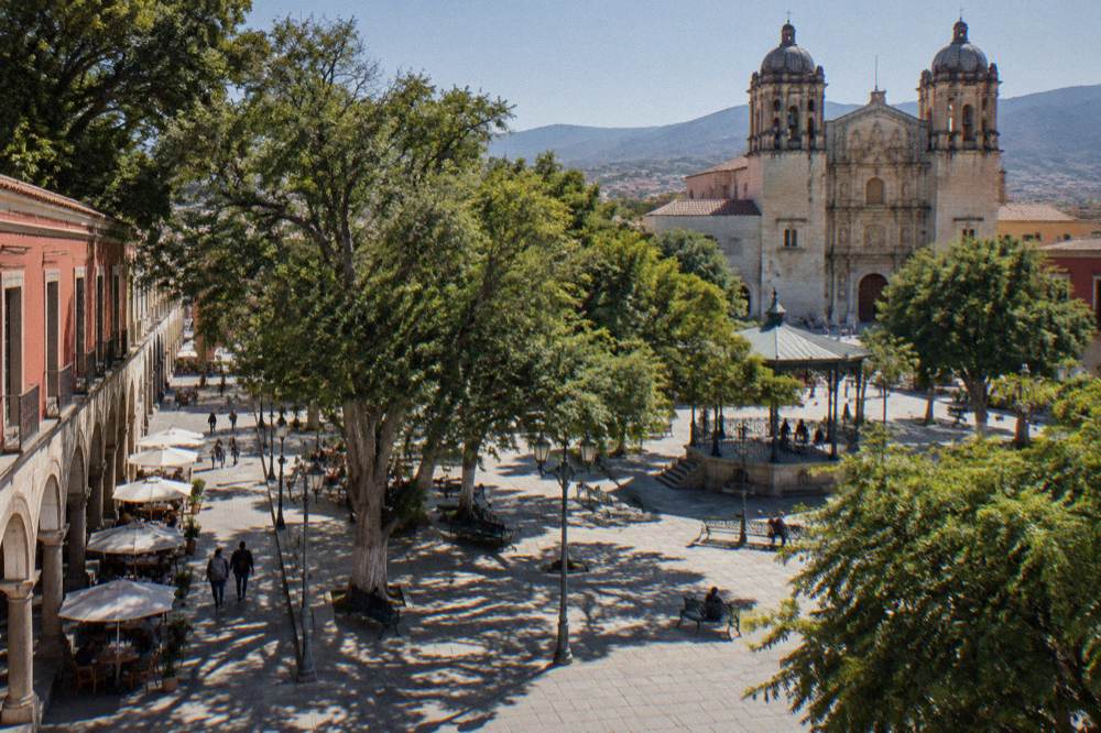 The Zócalo of Oaxaca City with trees, benches and the cathedral behind
