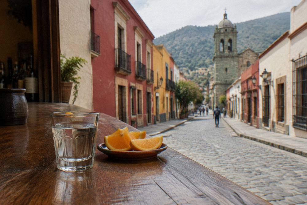 A glass of mezcal and orange slices on a wooden bar counter in Oaxaca City