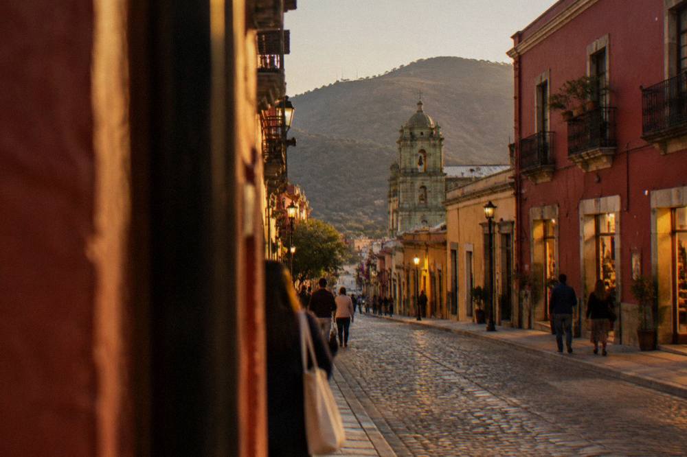 An evening street in Oaxaca City with lit shopfronts and people walking