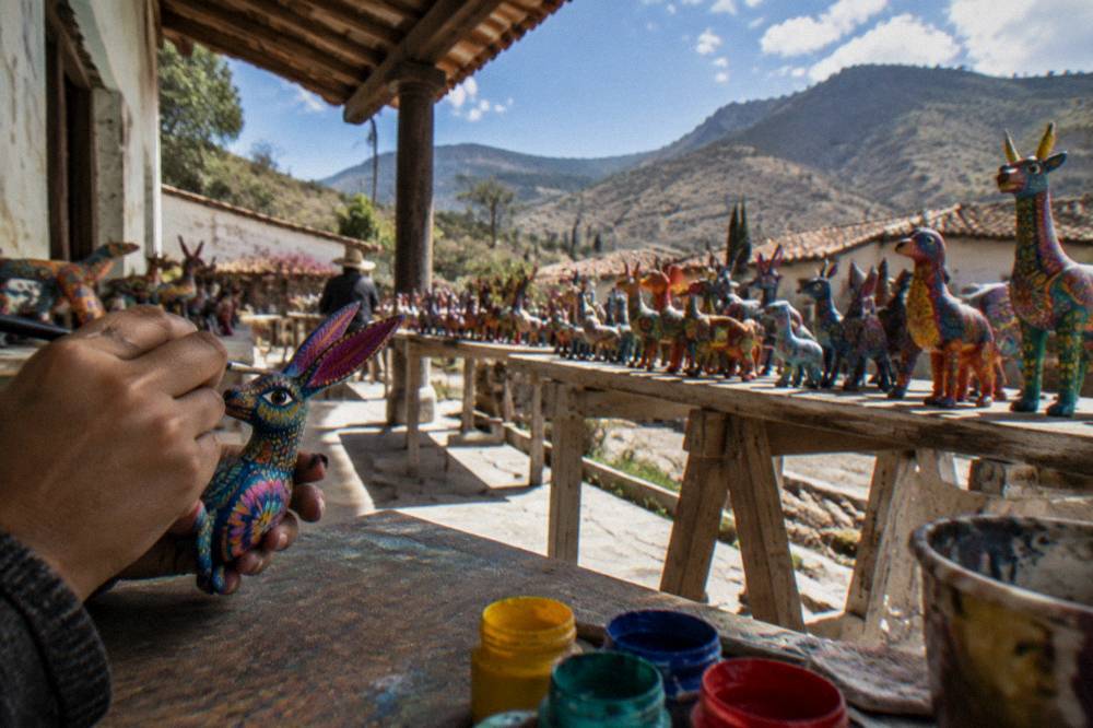 Hands painting a small carved alebrije figure at a workshop table