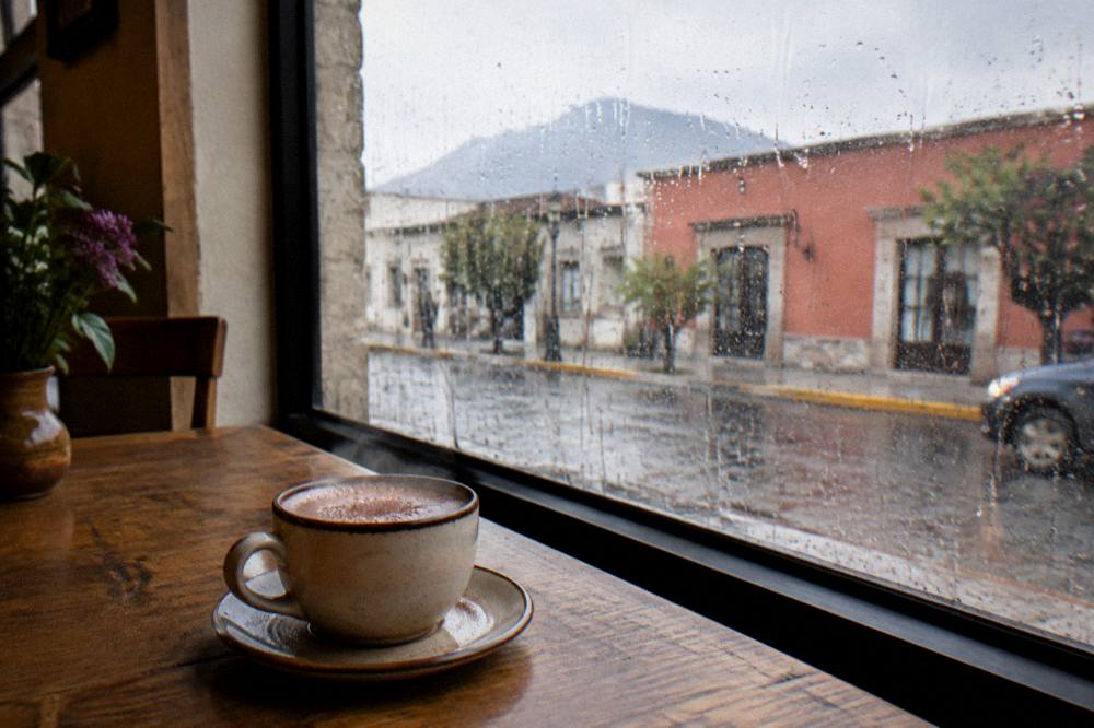 Café interior in Oaxaca with rain visible through the window and a cup of hot chocolate