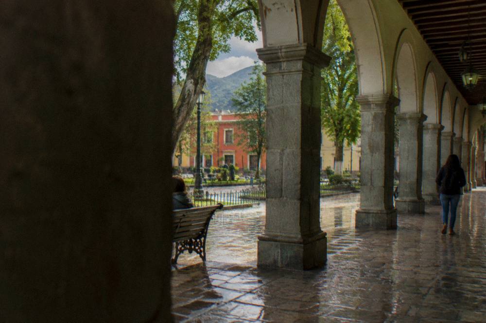 Rain falling on a colonial arcade while the street glows with reflected light