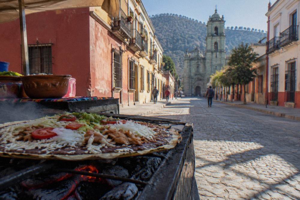 A market food stall in Oaxaca grilling a large tlayuda over open coals