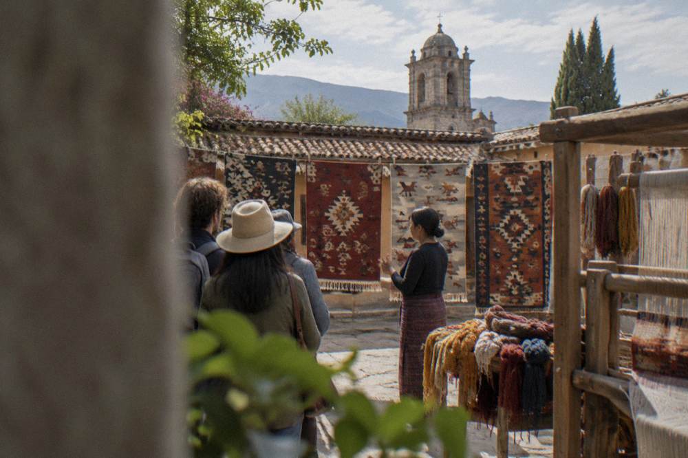 A guide explaining woven wool rugs to visitors inside a Teotitlán del Valle workshop