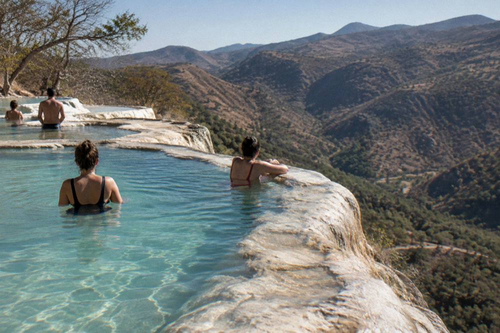 Visitors wading in the turquoise mineral pools at the edge of the Hierve el Agua cliffs