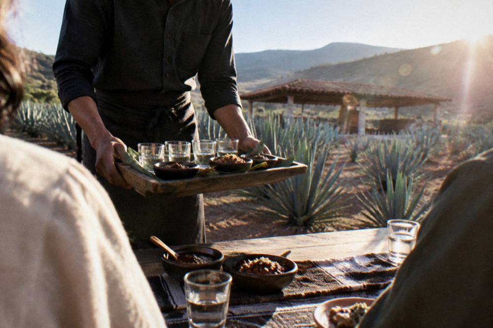 A sommelier presenting a tray of mezcal cups and small dishes of mole to guests at a pairing table