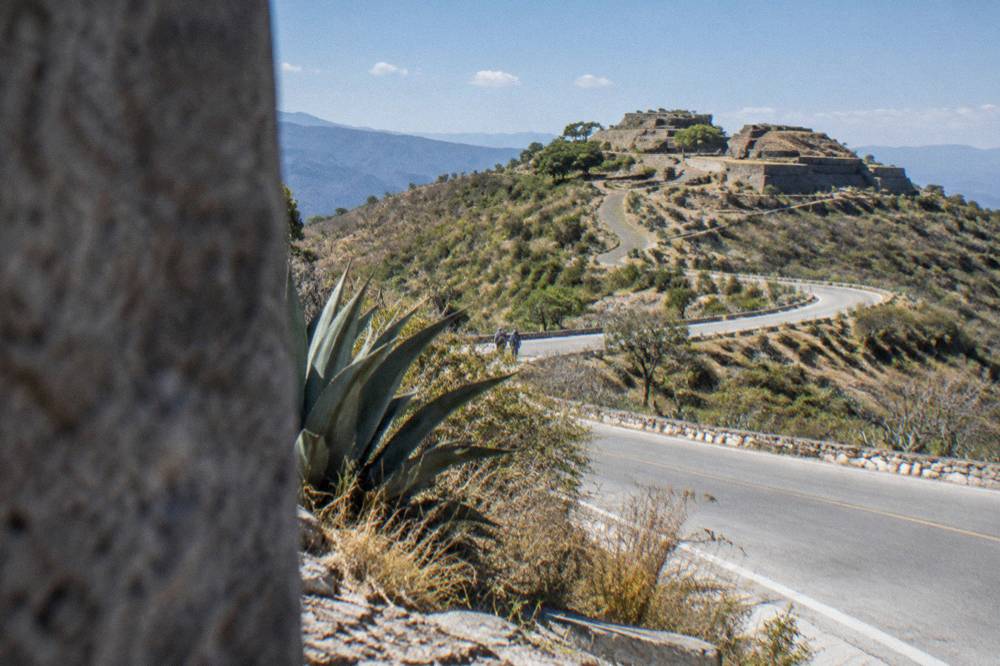 A winding mountain access road climbing toward an archaeological site on a hilltop