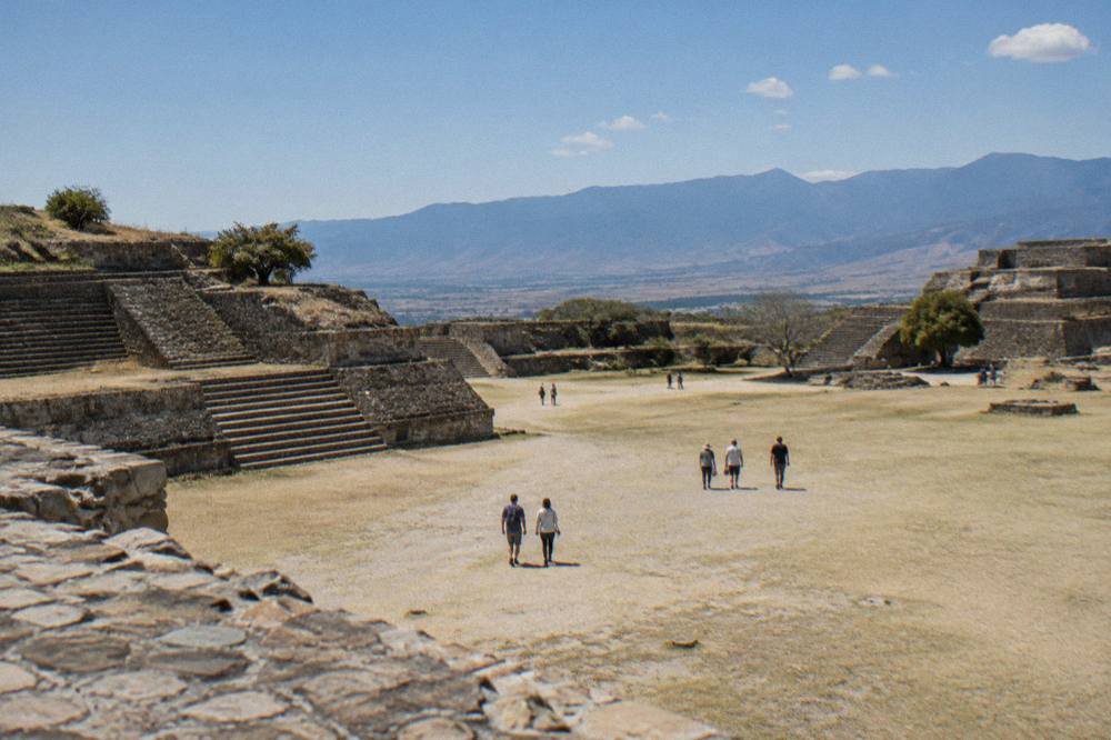 Visitors walking across an open stone plaza under afternoon sun