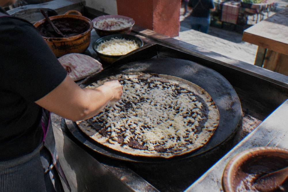 A large tlayuda being assembled with beans and cheese on a griddle