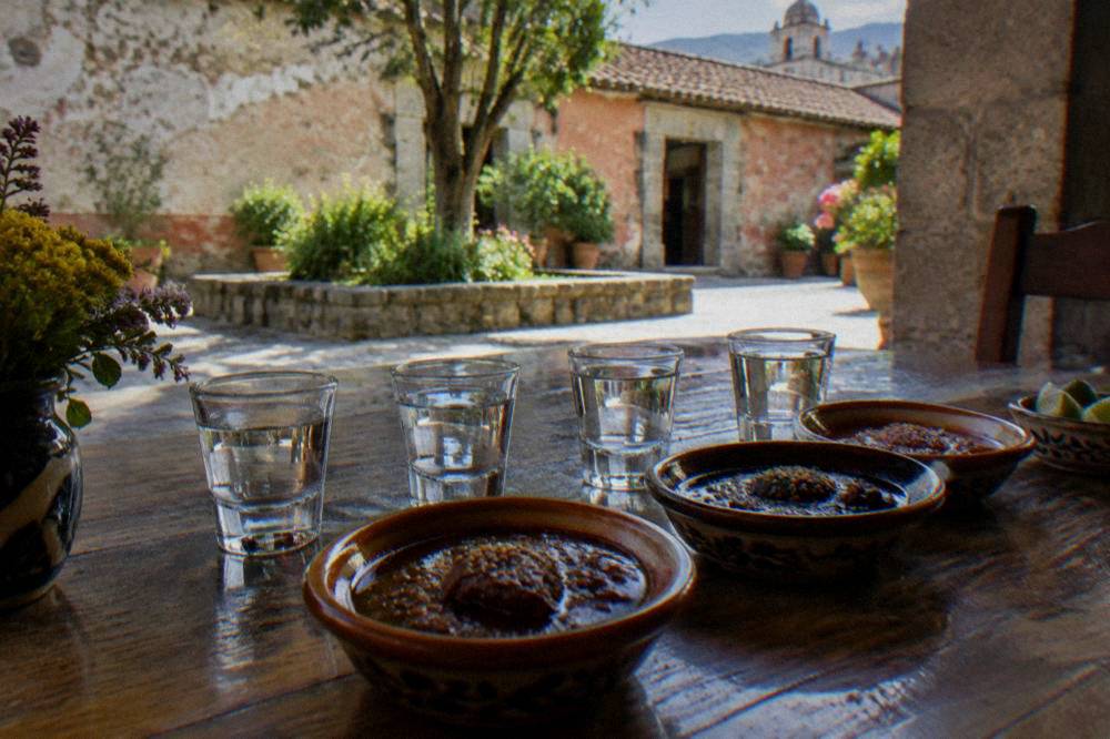 Glasses of mezcal lined up beside small dishes of mole