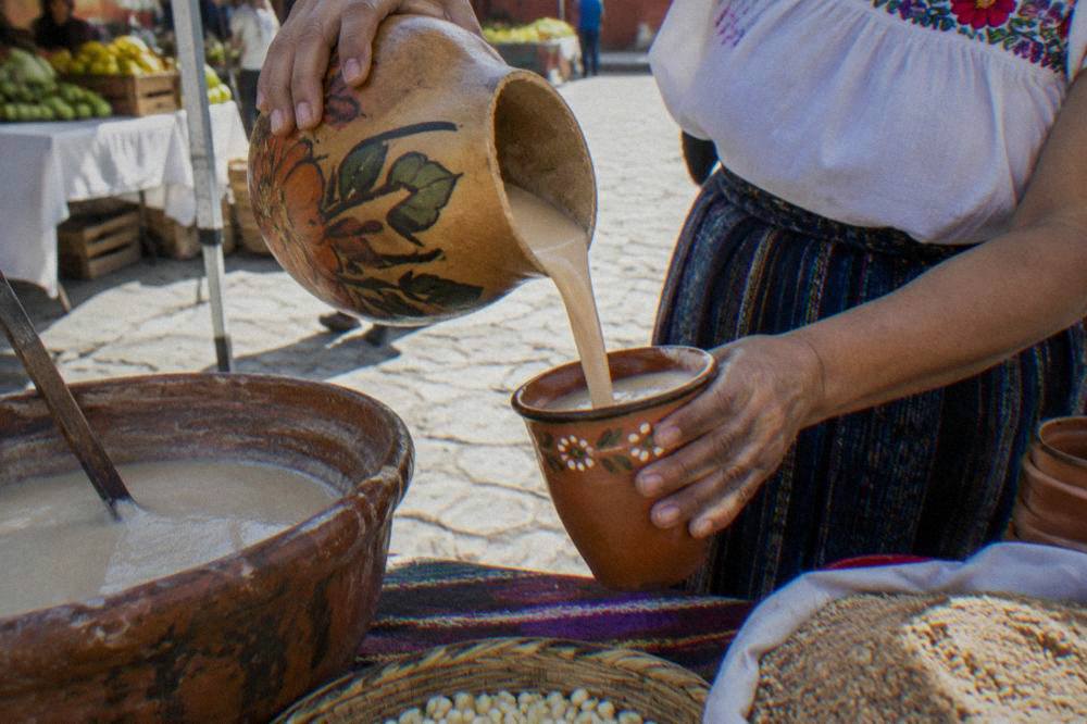 A vendor pouring tejate from a painted gourd into a cup