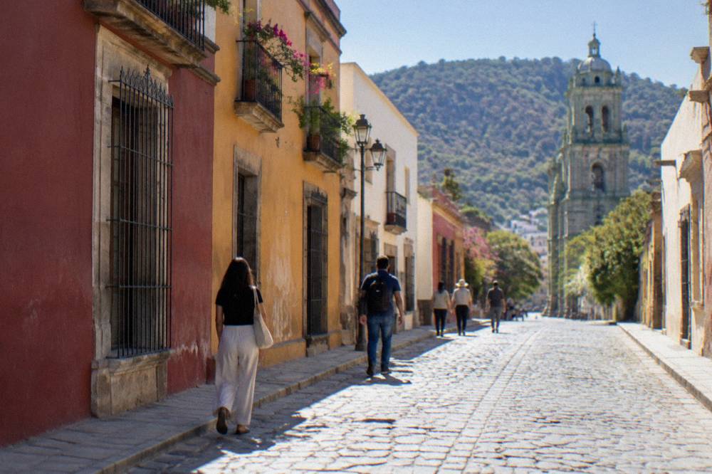 People walking along a cobbled street in Oaxaca City past coloured building fronts