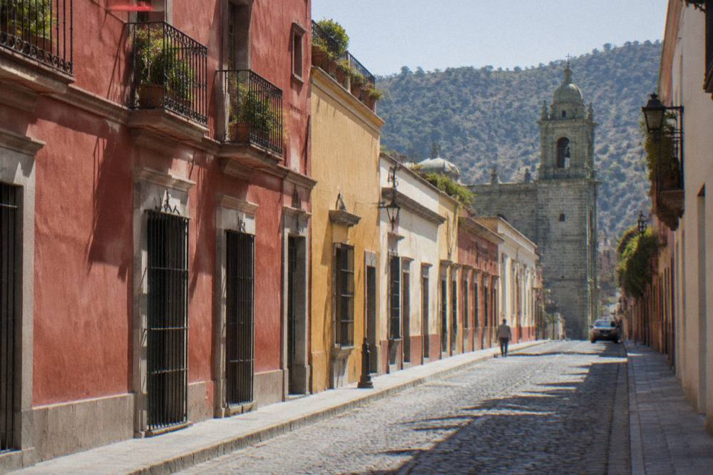 A quiet morning street in Oaxaca City with sunlight on old walls and closed shutters